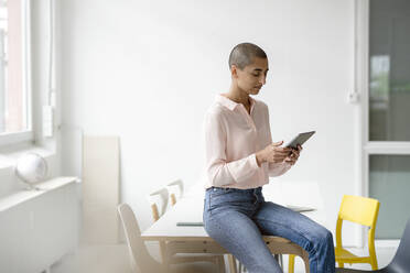 Businesswoman sitting on desk in loft office using tablet - KNSF08227