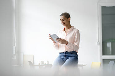 Geschäftsfrau sitzt auf einem Schreibtisch in einem Loft-Büro und benutzt ein Tablet - KNSF08228