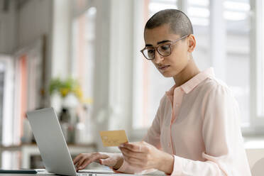 Geschäftsfrau, die eine Kreditkarte hält und einen Laptop am Schreibtisch in einem Loftbüro benutzt - KNSF08241