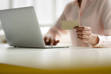 Close-up of businesswoman holding credit card and using laptop at desk in office - KNSF08242