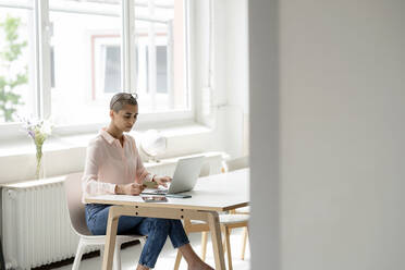 Businesswoman holding credit card and using laptop at desk in loft office - KNSF08243