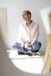 Porträt einer nachdenklichen Frau, die in einem Loft auf dem Boden sitzt - KNSF08260