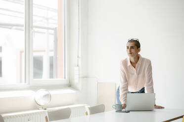 Businesswoman with laptop at desk in loft office - KNSF08269