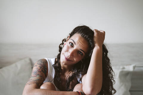 Young woman with hand in hair sitting against wall at home stock photo