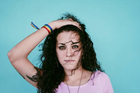 Close-up of smiling young woman with hand in hair against blue wall in city - EBBF00477