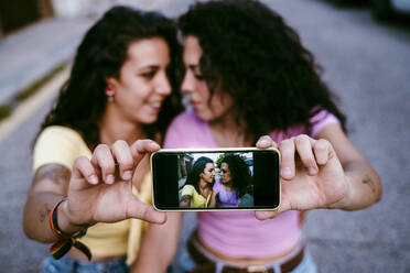 Nahaufnahme eines lesbischen Paares, das ein Selfie mit einem Smartphone in der Stadt macht - EBBF00504