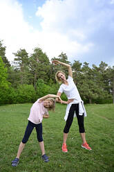 Mother with daughter stretching arms while standing on grassy land in forest - ECPF00984