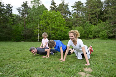 Family doing push-ups on grassy land against trees in forest - ECPF00986