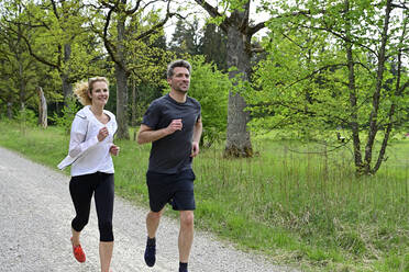 Couple running on dirt road against trees in forest - ECPF00996