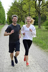 Happy couple running on dirt road against trees in forest - ECPF00997