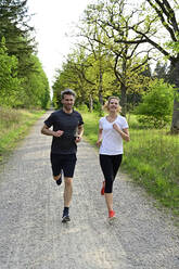 Happy couple jogging on dirt road against trees and plants in forest - ECPF00999