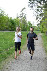 Happy couple jogging on dirt road against trees in forest - ECPF01000