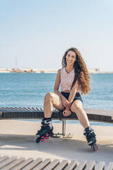 Junge Frau mit Inline-Skates auf einer Bank sitzend - DLTSF00883