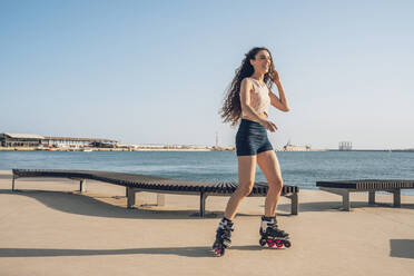 Young woman inline skating on promenade at the coast - DLTSF00884