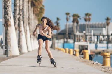 Young woman inline skating on promenade at the coast - DLTSF00886