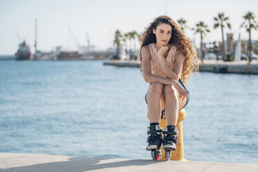 Junge Frau auf Inline-Skates sitzend auf Poller - DLTSF00887