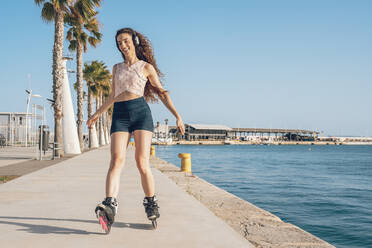 Junge Frau beim Inlineskaten auf der Promenade an der Küste - DLTSF00888