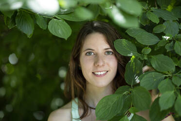 Nahaufnahme einer lächelnden jungen Frau bei Pflanzen im Wald - FLLF00500
