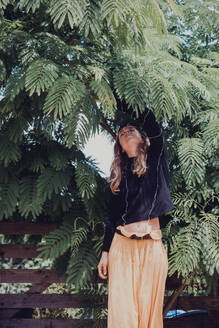 Frau mit geschlossenen Augen an einem Akazienbaum im Park - SKCF00666
