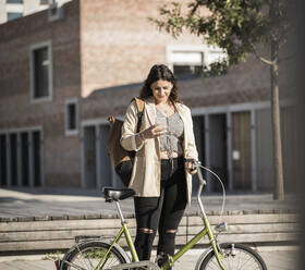 Junge Frau benutzt ihr Smartphone, während sie mit dem Fahrrad auf der Straße steht - UUF20758