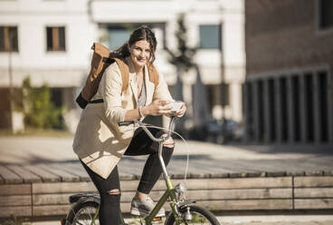 Weiblicher Pendler, der sein Smartphone benutzt, während er in der Stadt auf dem Fahrrad sitzt - UUF20762