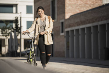 Lächelnder weiblicher Pendler mit Fahrrad auf der Straße in der Stadt - UUF20768