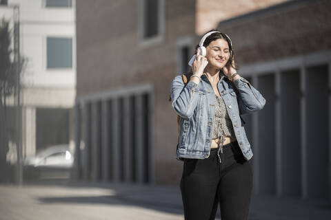 Smiling female commuter listening music through headphones while walking on street in city stock photo