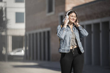 Smiling female commuter listening music through headphones while walking on street in city - UUF20774