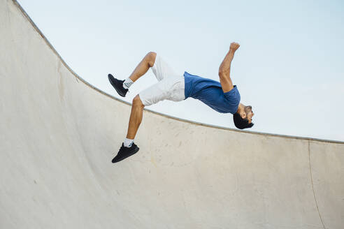 Junger Mann macht Wallflip auf Sportrampe gegen Himmel - MIMFF00097