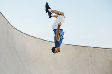 Upside down of young man doing wallflip on sports ramp against sky - MIMFF00098
