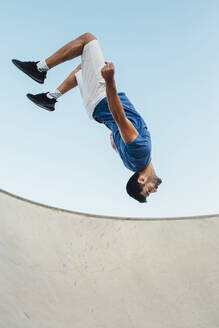 Young man doing wallflip over sports ramp against clear sky - MIMFF00099