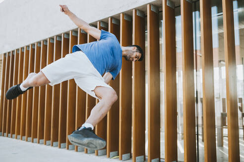 Young man performing stunt against built structure in city - MIMFF00110