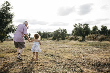 Grandfather with granddaughter walking on grassy land against sky - JRFF04660