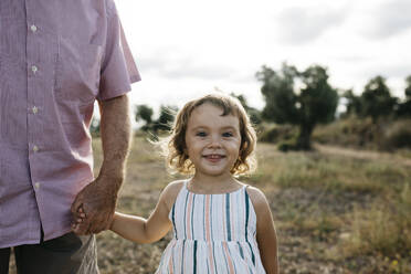 Lächelndes süßes Mädchen hält Großvaters Hand, während es auf dem Land steht - JRFF04662