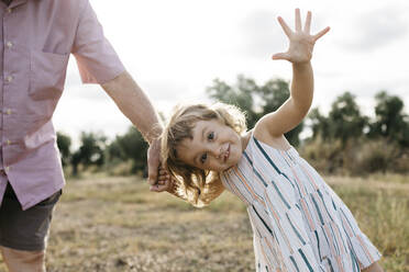 Cheerful cute girl holding grandfather's hand while standing on land against sky - JRFF04664