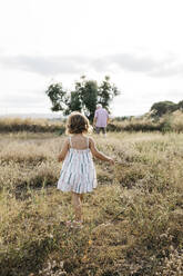 Grandfather and granddaughter walking on grassy land against sky - JRFF04666