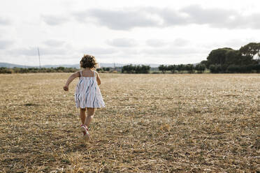 Girl running on grassy land against sky during sunny day - JRFF04667