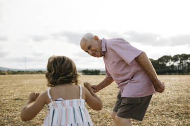 Grandfather looking at granddaughter while standing on land against sky - JRFF04668