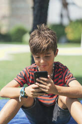 Boy using smart phone while sitting in yard - DLTSF00900