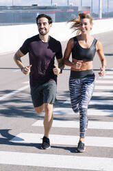 Smiling couple running on street in city during sunny day - JCMF01101