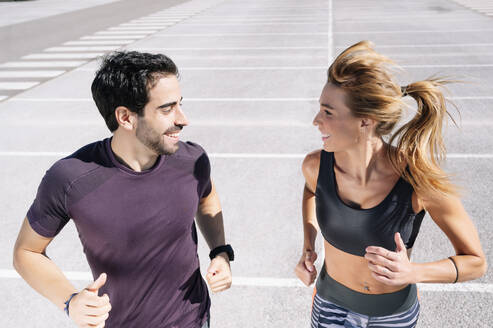 Smiling couple looking at each other while jogging on road in city - JCMF01118