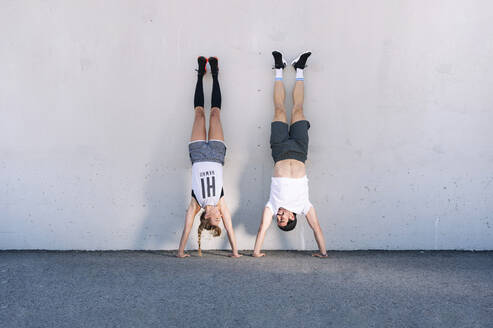 Couple doing handstands on road against wall in city - JCMF01129