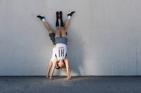 Couple doing handstands on street against wall in city stock photo