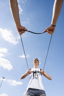 Couple exercising with strap against sky during sunny day - JCMF01134