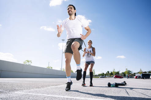 Couple exercising with strap while standing on road against sky during summer - JCMF01137