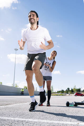 Cheerful couple exercising on street against sky during sunny day stock photo