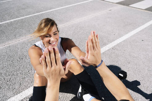Smiling woman giving high-five to boyfriend while exercising on road in city - JCMF01141