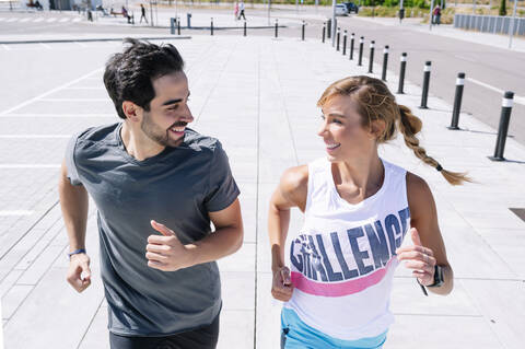 Smiling couple looking at each other while running on sidewalk in city stock photo