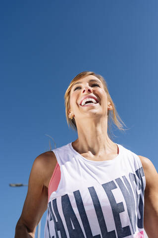 Mittlere erwachsene Frau lachend beim Laufen gegen einen klaren blauen Himmel an einem sonnigen Tag, lizenzfreies Stockfoto