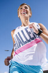 Cheerful woman running against clear blue sky during sunny day - JCMF01148